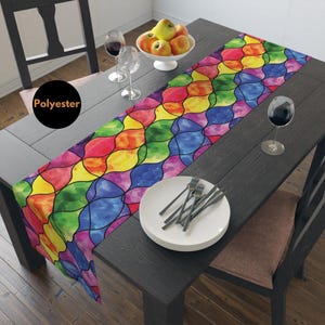 Puede incluir: Un camino de mesa colorido con un patrón de vitral en tonos de rojo, naranja, amarillo, verde, azul, morado y negro. El camino de mesa está hecho de poliéster y tiene 14 pulgadas (35,56 cm) de ancho.