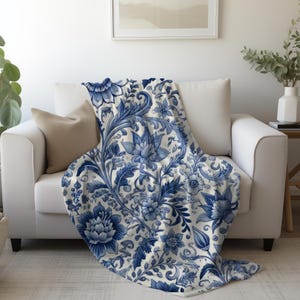 Puede incluir: Una manta de tiro blanca y azul con un patrón floral. El patrón presenta flores y hojas azules sobre un fondo blanco.