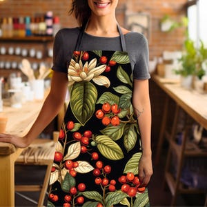 May include: A black apron with a floral print featuring red berries, green leaves, and white flowers. The apron has adjustable straps.