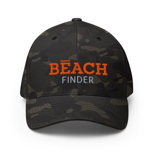 Può includere: Un cappellino da baseball mimetico con la scritta "BEACH FINDER" ricamata in arancione e bianco. Il cappellino ha una visiera curva e una vestibilità strutturata, adatta alle attività all'aperto.