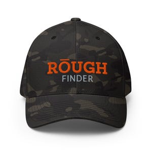 Può includere: Un cappellino da baseball mimetico con la scritta "ROUGH FINDER" in arancione e bianco. Il cappellino ha una visiera curva e una vestibilità strutturata. Il cappello è realizzato in un materiale resistente ed è adatto alle attività all'aperto.