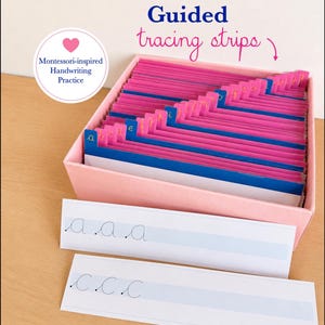 May include: A pink box containing blue and pink alphabet tracing strips with tabs labeled a through z. Two white paper strips with cursive letter practice for a and c are placed in front. Text reads Guided tracing strips and Montessori-inspired Handwriting Practice.
