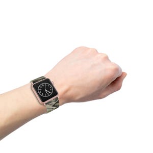 May include: A rose gold Apple Watch with a camouflage patterned band. The watch face is black with white numbers.