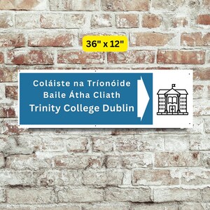 May include: A rectangular sign, 36" x 12", with a blue background and white text that reads "Coláiste na Tríonóide Baile Átha Cliath Trinity College Dublin." A white arrow points right toward a black and white illustration of a building.