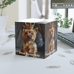 Puede incluir: Un bloc de notas cuadrado con un Yorkshire Terrier que lleva una corona dorada. El perro es marrón y negro con una expresión regia. El bloc de notas tiene el texto "Print it your way" en la parte delantera.