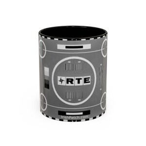 May include: A ceramic mug with a black interior and a gray exterior featuring a test pattern design. The design includes the letters "RTE" within a circle, along with various bars and shapes. The website "IrishPatch.com" is printed at the bottom.