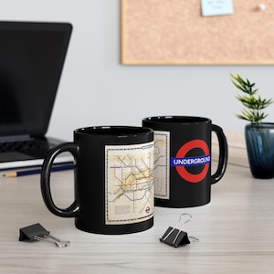 May include: Two black ceramic mugs. One mug features a vintage London Underground map design. The other mug has the London Underground logo, a red circle with a blue bar that reads "UNDERGROUND".