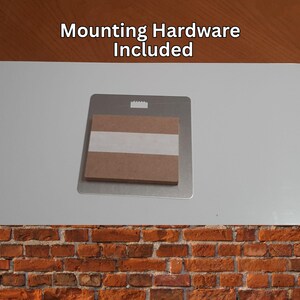 Peut inclure: Un support de montage en m&eacute;tal avec un dos en carton et du ruban adh&eacute;sif. Le texte "Mounting Hardware Included" est imprim&eacute; en haut. Le support est con&ccedil;u pour le montage mural.