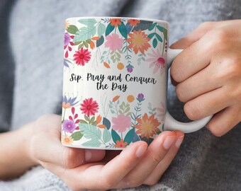 May include: White ceramic mug with a floral pattern and the text "Sip, Pray and Conquer the Day".