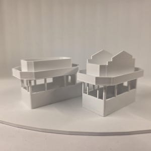 May include: Two white, miniature architectural models. One has a flat roof, the other has a stepped roof design. Both have a rectangular base with open sides and a second-level platform. The models are displayed on a white circular surface.