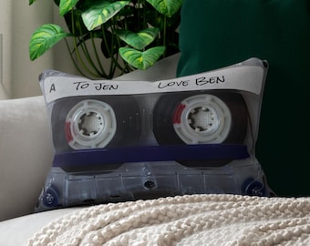 May include: A white cassette tape pillow with the text "A to Jen Love Ben" printed on it. The pillow is on a white blanket.