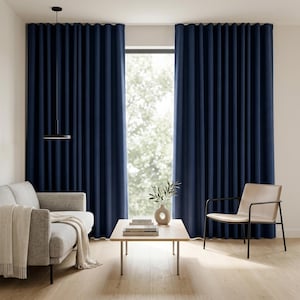 Könnte beinhalten: Marineblaue, bodenlange Vorhänge rahmen ein Fenster mit Blick ins Grüne ein. Ein graues Sofa mit cremefarbenem Überwurf, ein Holztisch und ein moderner Stuhl vervollständigen das Wohnzimmer. Eine schwarze Pendelleuchte hängt von der Decke.