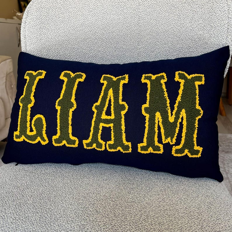 Custom punch needle name pillow reading Liam, styled in a cozy bohemian home setting with neutral tones, perfect for new home decoration.