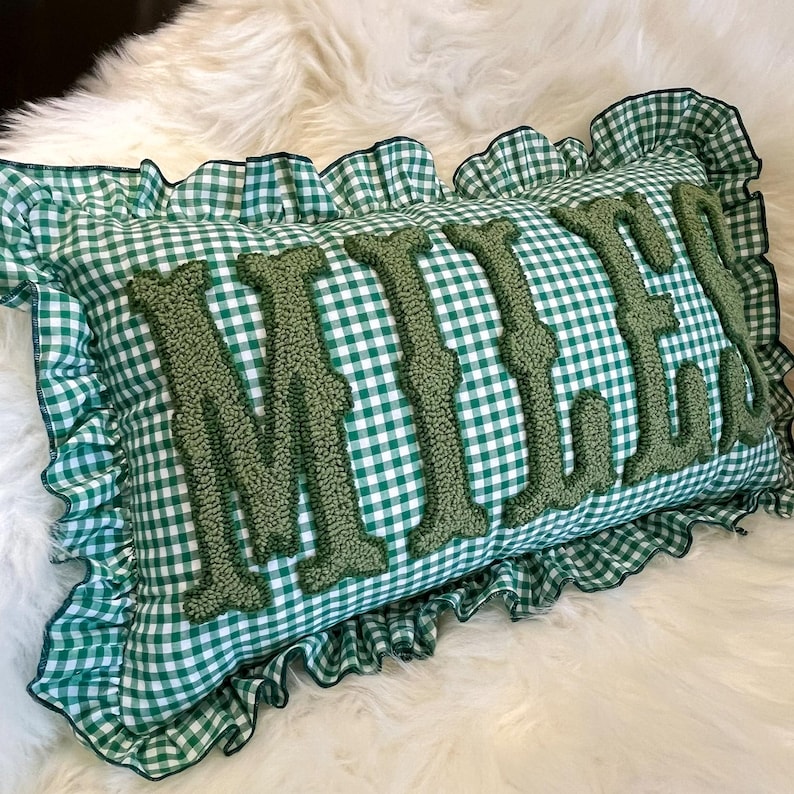 May include: A rectangular cushion with a green and white gingham pattern. The word "MILES" is embroidered in a textured green font across the centre. The cushion has a ruffled edge in the same gingham fabric.