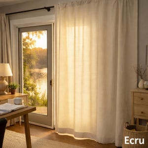 Può includere: Pannello di tenda in lino color ecru appeso davanti a una porta a vetri. La tenda è realizzata in un tessuto strutturato ed è leggermente traslucida, permettendo alla luce del sole di filtrare. La parola "Ecru" è visibile in basso a destra.