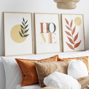 May include: Three framed prints with a minimalist design. The prints feature a yellow circle with a green leaf, the word "HOME" in a layered font, and a red leaf with a yellow circle.