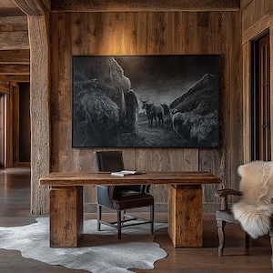 May include: A rustic home office with wood paneling and a large wooden desk. A black and white painting of cattle hangs above the desk. A cowhide rug and a chair with a sheepskin throw complete the space.