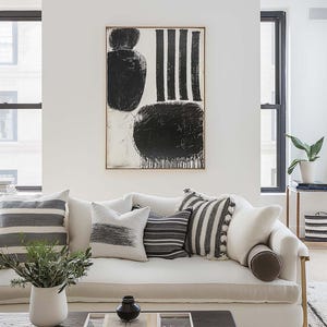 Pode incluir: Um sofá de linho branco com almofadas listradas em preto e branco e uma pintura abstrata em preto e branco na parede atrás.