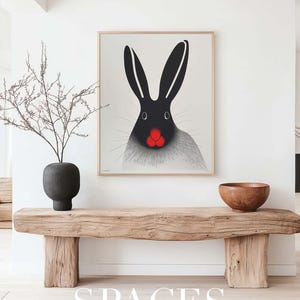 Puede incluir: Una impresi&oacute;n enmarcada de un conejo blanco y negro con la nariz roja, colgada en una pared blanca sobre un banco de madera. El banco est&aacute; en una habitaci&oacute;n con una pared blanca y un suelo de madera. El texto "SPACES FINE ART MOCKUPS" est&aacute; impreso debajo del banco.