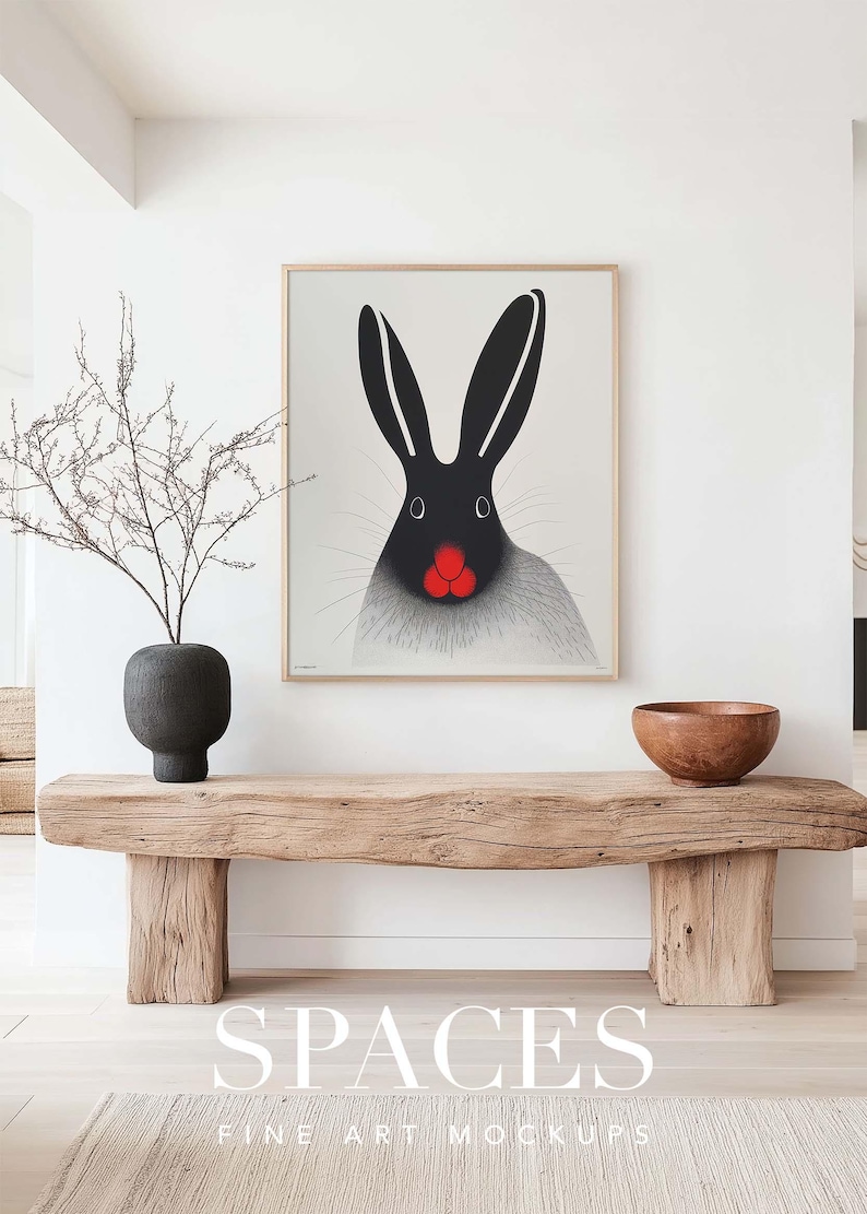 Puede incluir: Una impresi&oacute;n enmarcada de un conejo blanco y negro con la nariz roja, colgada en una pared blanca sobre un banco de madera. El banco est&aacute; en una habitaci&oacute;n con una pared blanca y un suelo de madera. El texto "SPACES FINE ART MOCKUPS" est&aacute; impreso debajo del banco.