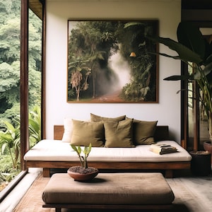 May include: A white futon with brown wooden legs and a white cushion. The futon is in a room with a large window, a framed picture of a jungle scene, and a small potted plant on a brown wooden coffee table.
