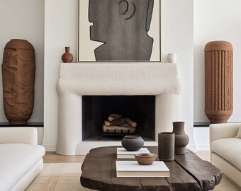 May include: A living room interior with a white fireplace, a wooden coffee table, two white sofas, and two tall brown ceramic vases. A black and white abstract art print hangs above the fireplace.