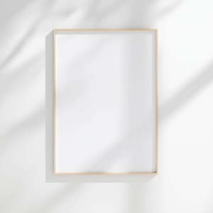 Puede incluir: Un marco de fotos rectangular y vacío con un borde de madera fino y de color claro. El marco está centrado en una pared blanca, con sombras de follaje que añaden un elemento natural. Listo para una obra de arte o una fotografía.