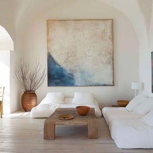 May include: A light and spacious living room with white walls, a wooden floor, and an abstract painting with blue and beige hues. The room includes low seating, a wooden coffee table, and a large terracotta vase.