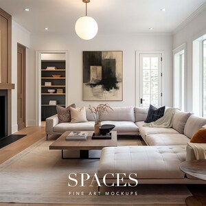May include: A white sectional sofa with a gray throw blanket and a black and white abstract painting hanging above it. The sofa is in a living room with a wooden floor and a coffee table with books and a vase of flowers.