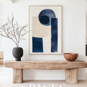 Puede incluir: Un banco de madera con un jarr&oacute;n de ramas secas y un cuenco de madera en la parte superior. Un cuadro abstracto enmarcado con formas azules y beige cuelga de la pared sobre el banco. El texto "SPACES FINE ART MOCKUPS" est&aacute; impreso debajo del banco.