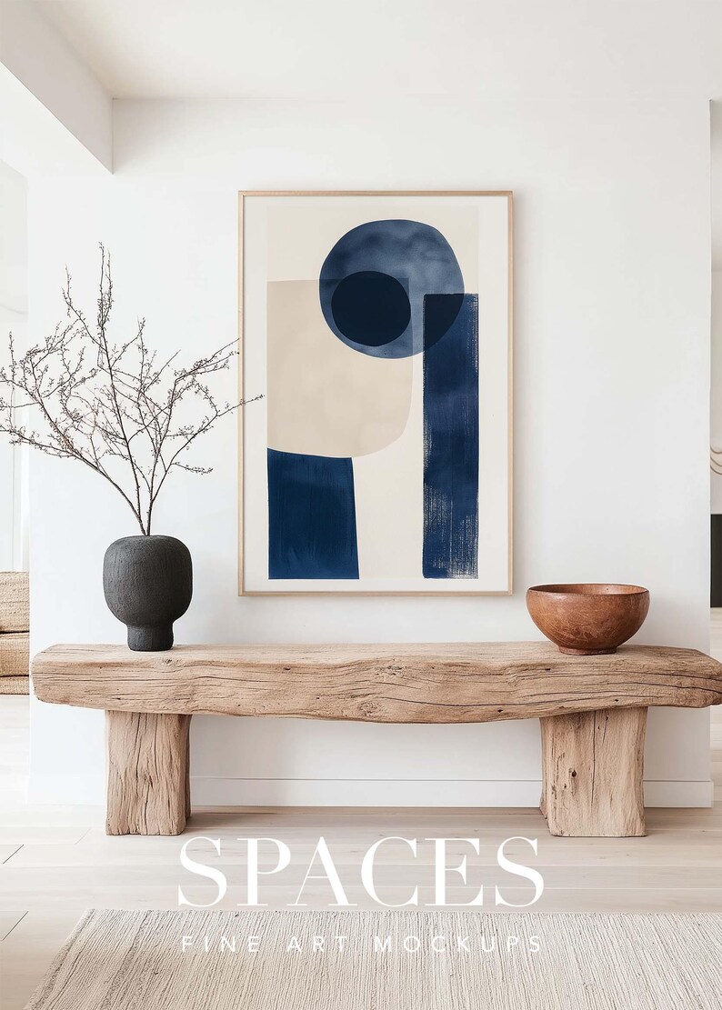 Puede incluir: Un banco de madera con un jarr&oacute;n de ramas secas y un cuenco de madera en la parte superior. Un cuadro abstracto enmarcado con formas azules y beige cuelga de la pared sobre el banco. El texto "SPACES FINE ART MOCKUPS" est&aacute; impreso debajo del banco.
