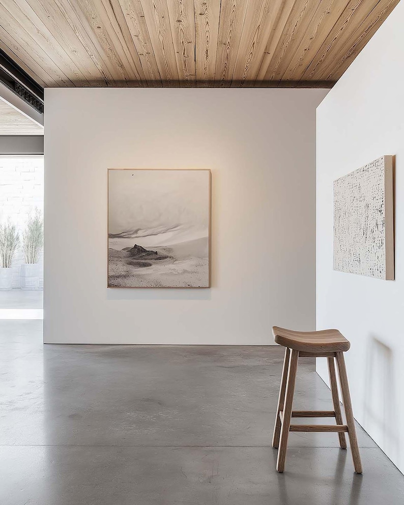 May include: A modern interior featuring a wooden stool with a curved seat and four legs. The room has white walls, a concrete floor, and a framed landscape artwork. The ceiling is made of wooden planks.