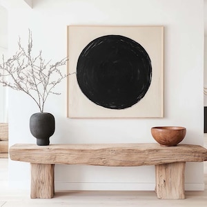 Puede incluir: Un banco de madera rústico con un acabado de madera natural se encuentra en un interior minimalista. Un cuadro abstracto en blanco y negro cuelga de la pared sobre el banco. Un jarrón negro con una rama seca se encuentra sobre el banco. Un cuenco de madera se encuentra sobre el banco.