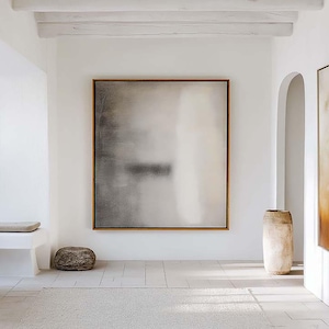 Puede incluir: Interior luminoso y minimalista con paredes blancas y suelo de baldosas. Grandes pinturas abstractas en tonos neutros cuelgan de las paredes. Un banco de madera y una escultura de piedra añaden textura. Un jarrón grande está cerca de una puerta arqueada.