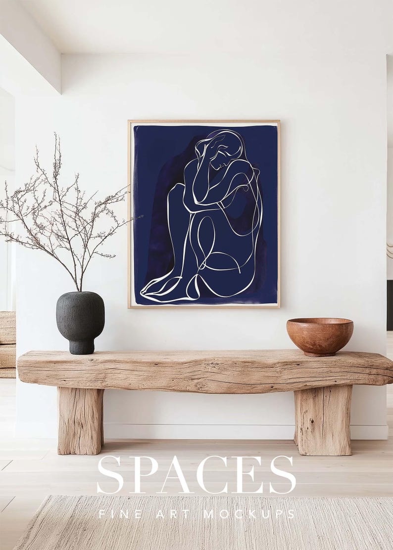 Puede incluir: Un banco de madera con una impresi&oacute;n enmarcada en azul oscuro de un dibujo lineal de una persona sobre un fondo blanco. La impresi&oacute;n est&aacute; colgada en una pared blanca. Un peque&ntilde;o jarr&oacute;n con una rama seca est&aacute; en el banco. Un cuenco de madera est&aacute; en el banco a la derecha de la impresi&oacute;n. El texto "SPACES FINE ART MOCKUPS" est&aacute; en la parte inferior de la imagen.