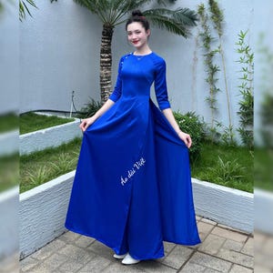 May include: A royal blue long-sleeved dress with a high neckline and a side slit. The dress has a fitted bodice and a flowing skirt. The dress is embroidered with the text "Ao dai Viet".