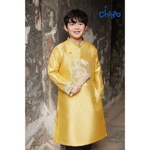 May include: A young person wearing a golden yellow traditional tunic with a dragon design. The tunic has long sleeves and a mandarin collar. The person is holding a fan. The brand logo "Chippo" is visible in the top right corner.