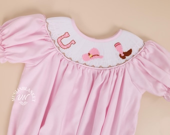 Könnte beinhalten: Rosafarbenes Babykleid mit einem weißen bestickten Kragen, der ein Hufeisen, einen Cowboyhut und einen Stiefel zeigt.