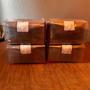 May include: Four rectangular mushroom cultivation bags stacked in two columns. Each clear plastic bag contains a dark brown substrate and features a white circular filter patch centered on the front side for air exchange and gas regulation.