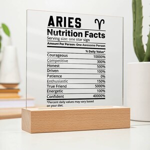 May include: A clear acrylic sign with a wood base, featuring a nutrition facts label for the zodiac sign Aries. The sign lists traits like courageous, competitive, honest, driven, and confident with corresponding percentages.