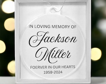 May include: A clear round ornament with a black ribbon and the text "In loving memory of Jackson Miller Forever in our hearts 1959-2024".