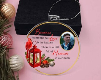 May include: A pink round Christmas ornament with a gold border. The ornament features a cardinal, a lantern, pine cones, and a small Christmas tree. The ornament also has a photo of an older man and the text "Because someone we love is in heaven, there is a little bit of heaven in our home."