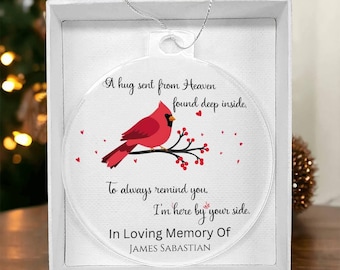May include: A clear glass ornament with a red cardinal perched on a branch with red berries. The ornament has the text "A hug sent from Heaven found deep inside. To always remind you. I'm here by your side. In Loving Memory Of JAMES SABASTIAN".