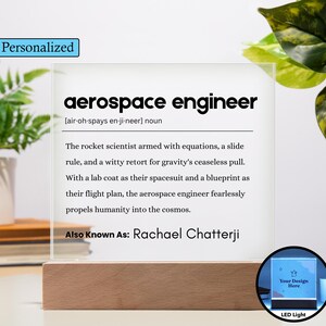 May include: A personalized LED light with a wooden base. The clear acrylic panel features the definition of "aerospace engineer" and the text "Also Known As: Rachael Chatterji". The light has a small, round design area that says "Your Design Here".