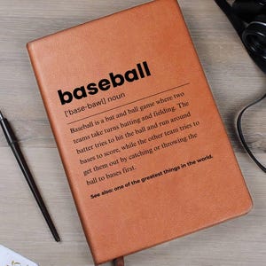 May include: A brown leather-bound notebook with the word "baseball" in bold black letters. The definition of baseball is printed below the title. A pen, binoculars, and a small envelope are also visible.