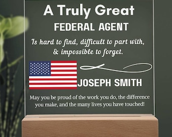 May include: A clear acrylic plaque with the text "A Truly Great FEDERAL AGENT" and a US flag. The plaque sits on a wooden base and includes the name "JOSEPH SMITH". The text reads "Is hard to find, difficult to part with, & impossible to forget."