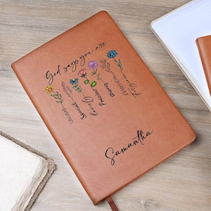 May include: A brown leather journal with the text "God says you are" and a floral design. The words "loved, precious, strong, special, unique" are written on the flowers. The name "Samantha" is written at the bottom of the journal.