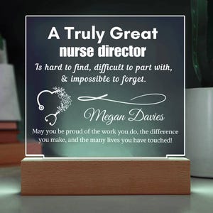 Może przedstawiać: Podświetlana tablica akrylowa z napisem "A Truly Great nurse director" i spersonalizowaną wiadomością. Tablica ma drewnianą podstawę i sercowaty wzór ze stetoskopem. Tekst jest biały.