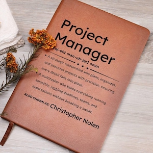 Puede incluir: Un diario de cuero marrón con el texto "Project Manager" y una definición del término. El texto también incluye el nombre "Christopher Nolen" en la parte inferior.