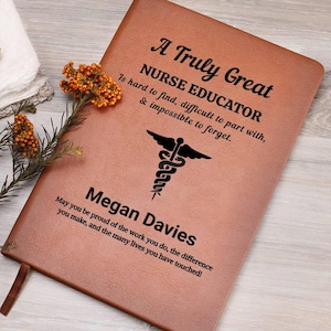 May include: A brown leather journal with the text "A Truly Great Nurse Educator" and a medical symbol. The journal is personalized with the name "Megan Davies" and a heartfelt message. A sprig of orange flowers rests near the journal.